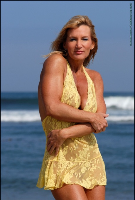Muscular blonde Peggy Vee frees her fake tits from a yellow dress at the ocean