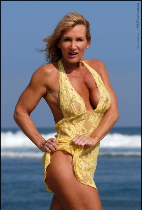 Muscular blonde Peggy Vee frees her fake tits from a yellow dress at the ocean